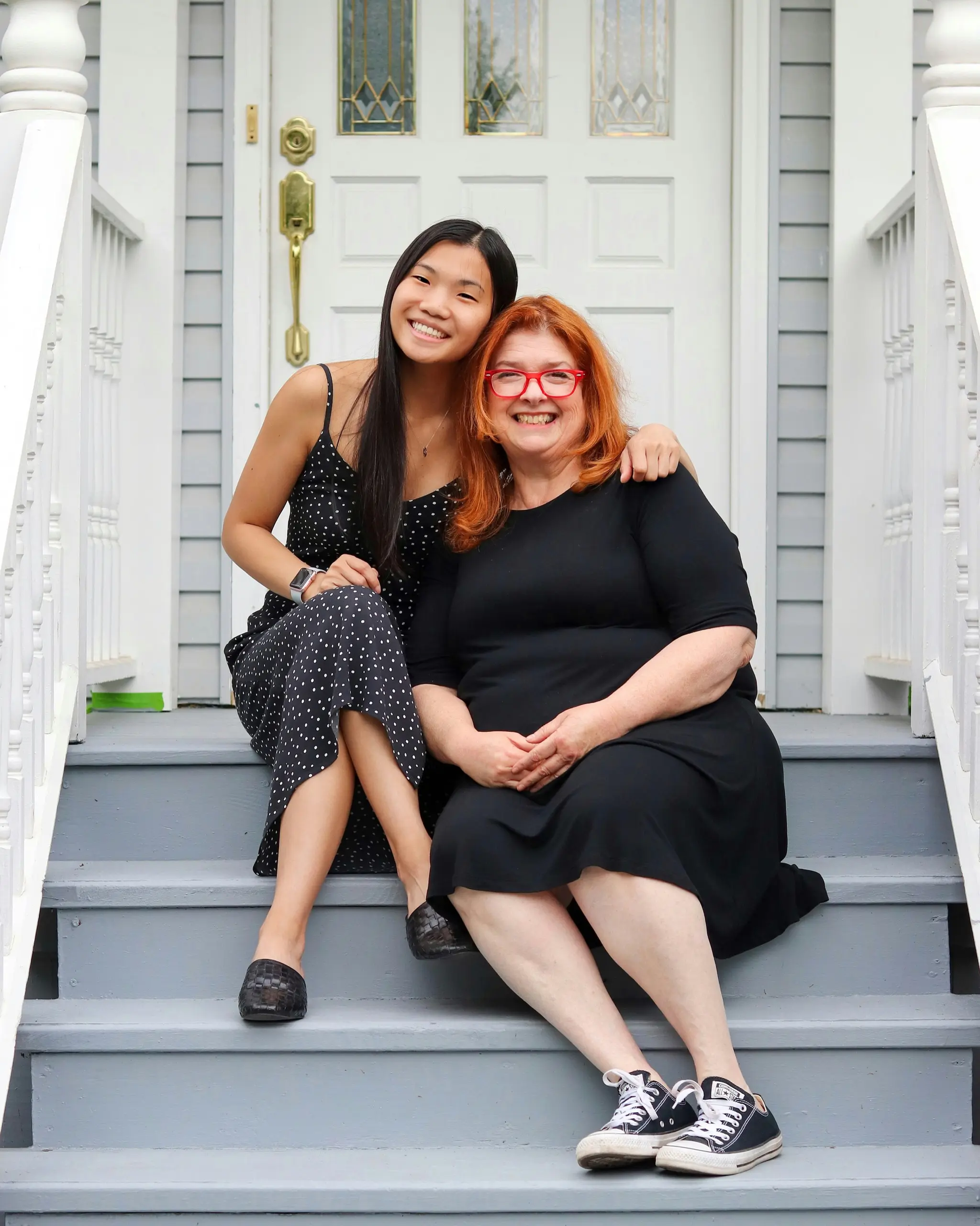 Dos mujeres ríen juntas en los escalones de la entrada de una casa