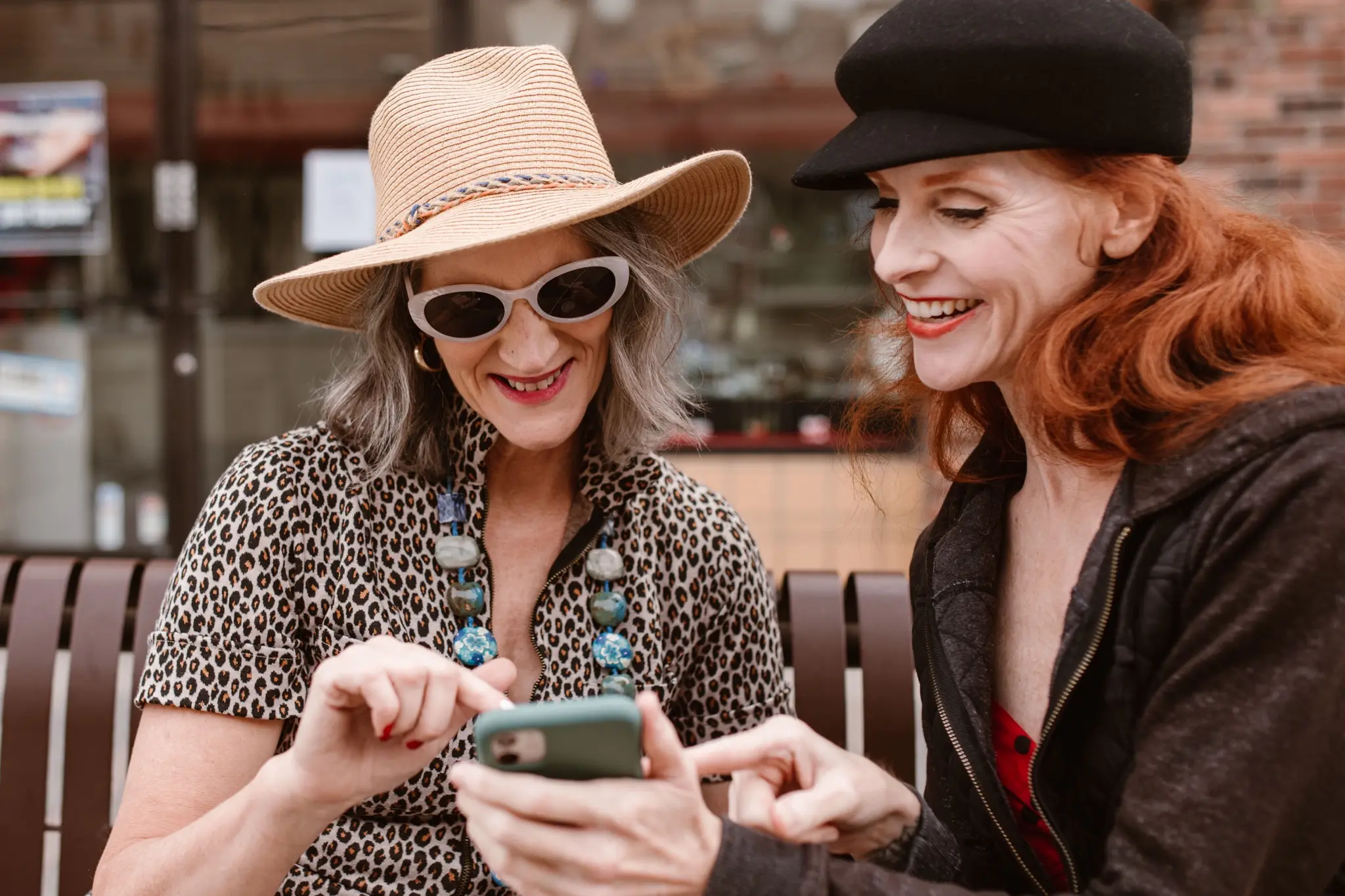 Dos mujeres ríen juntas mirando un teléfono en una banca de la ciudad